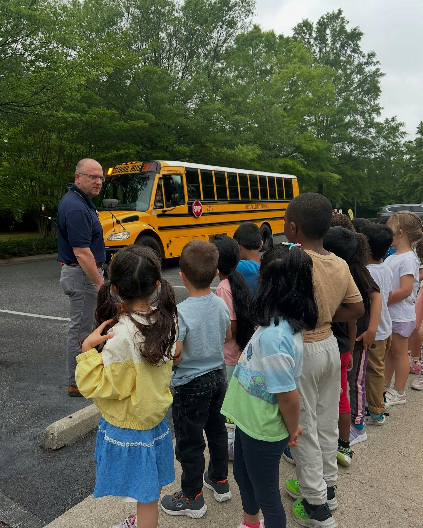 Adult speaking to a line of children in front of a school bus
