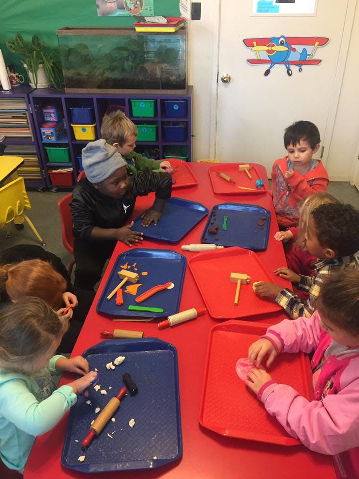 Children playing with modeling clay and tools at a red table