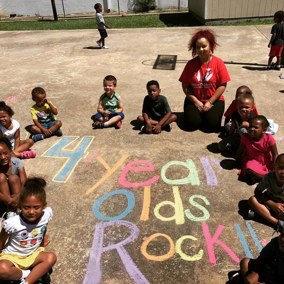 Adult and children sitting around chalk writing that says "4 Year Olds Rock!"