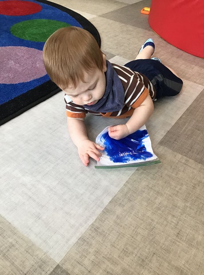 Child on floor playing with a bag of blue paint