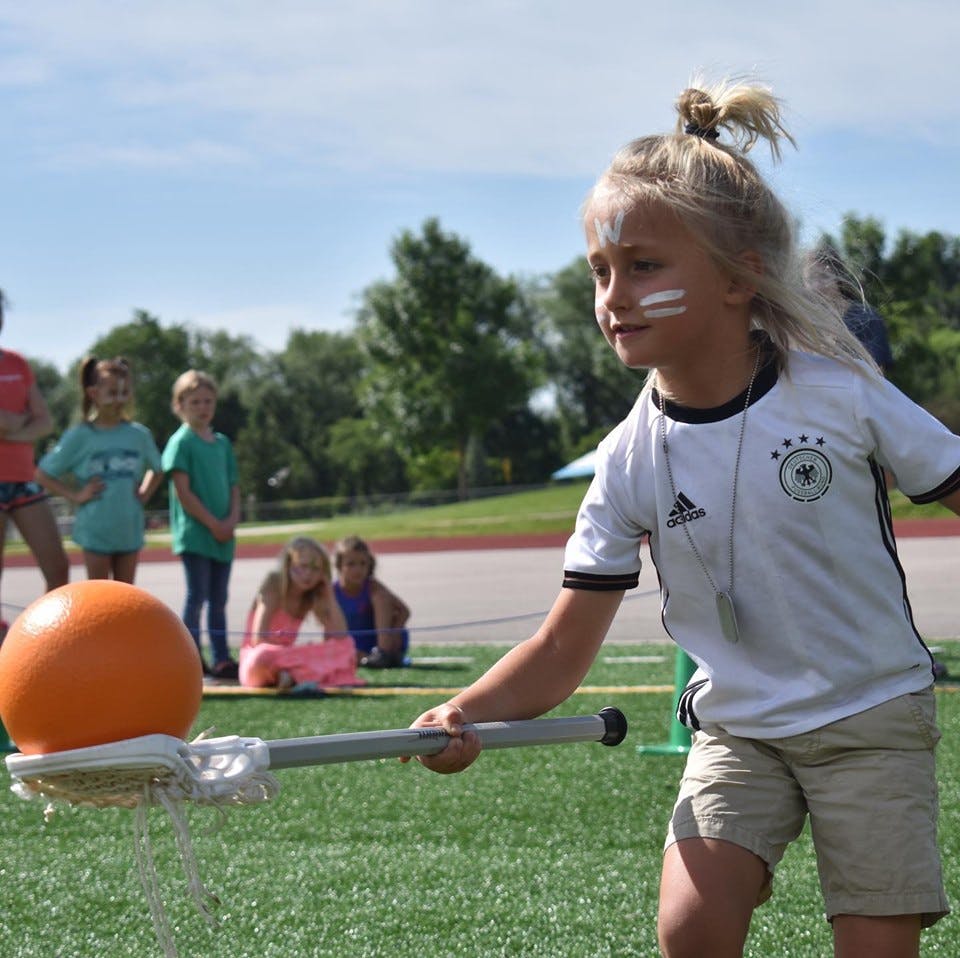 Child with face paint holding a lacrosse stick with an orange ball