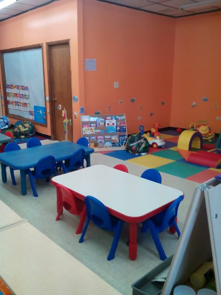 Classroom with small tables and chairs, colorful floor mats, and toys