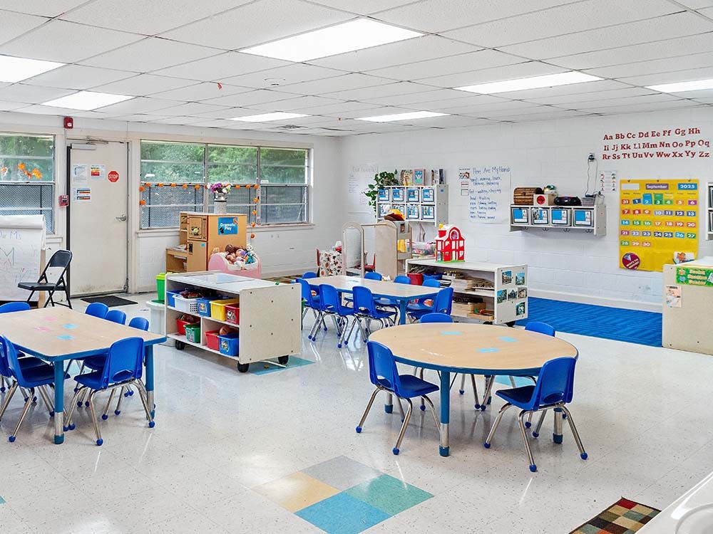 Classroom with small tables, blue chairs, and alphabet on the wall