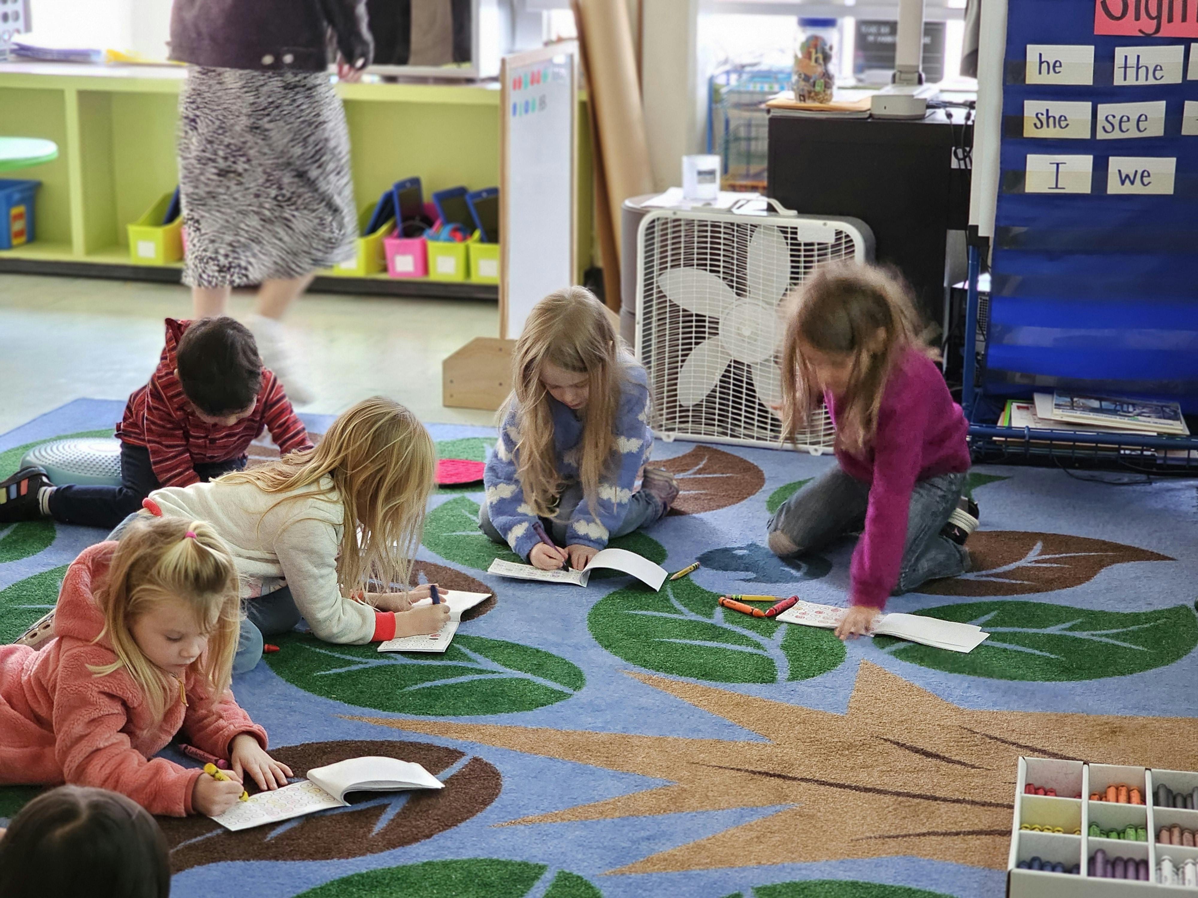 Children writing and drawing on a patterned rug in a classroom