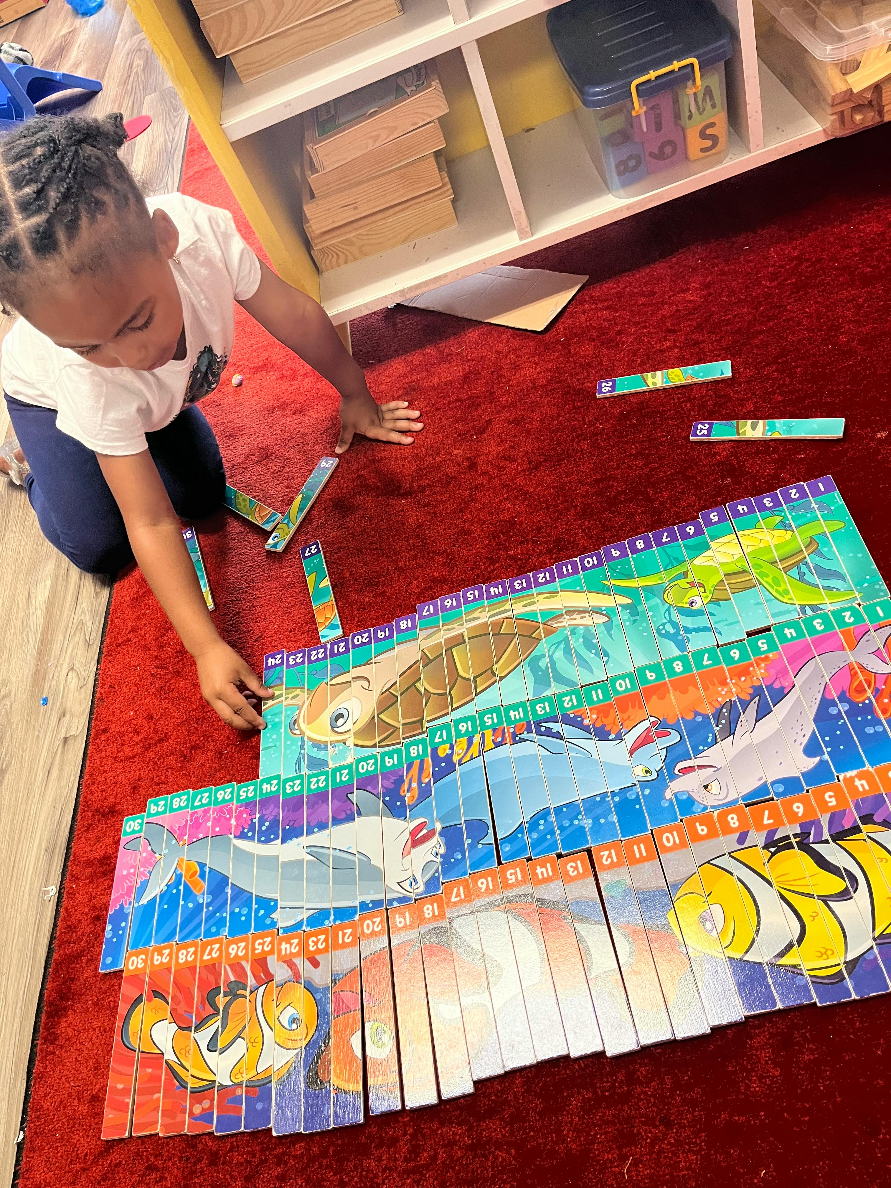 Child on a red rug assembling a floor puzzle with ocean animals