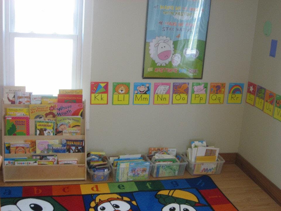 Bookshelf with books, alphabet cards on wall, and colorful rug in a classroom