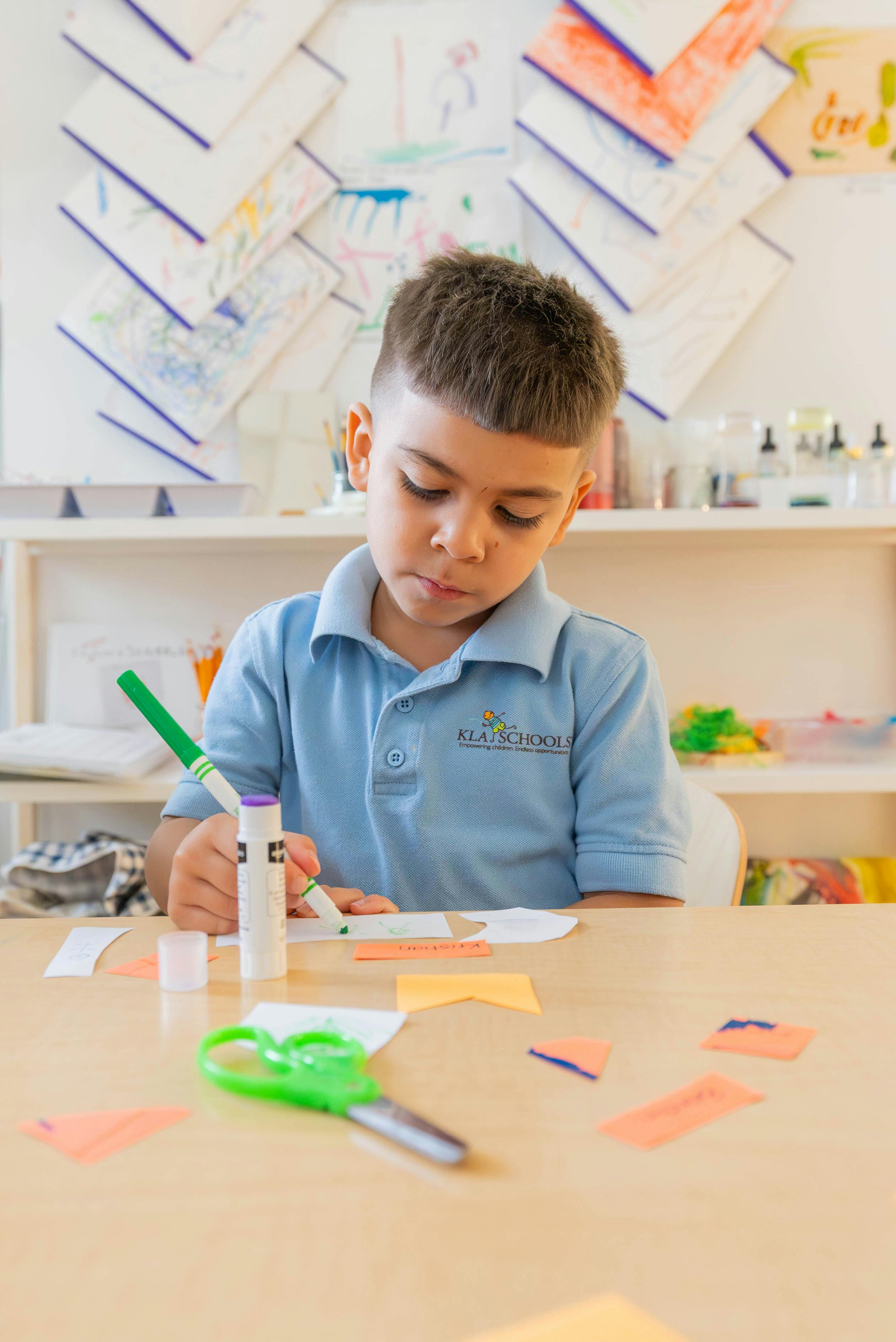 Child coloring with a green marker at a table in a classroom