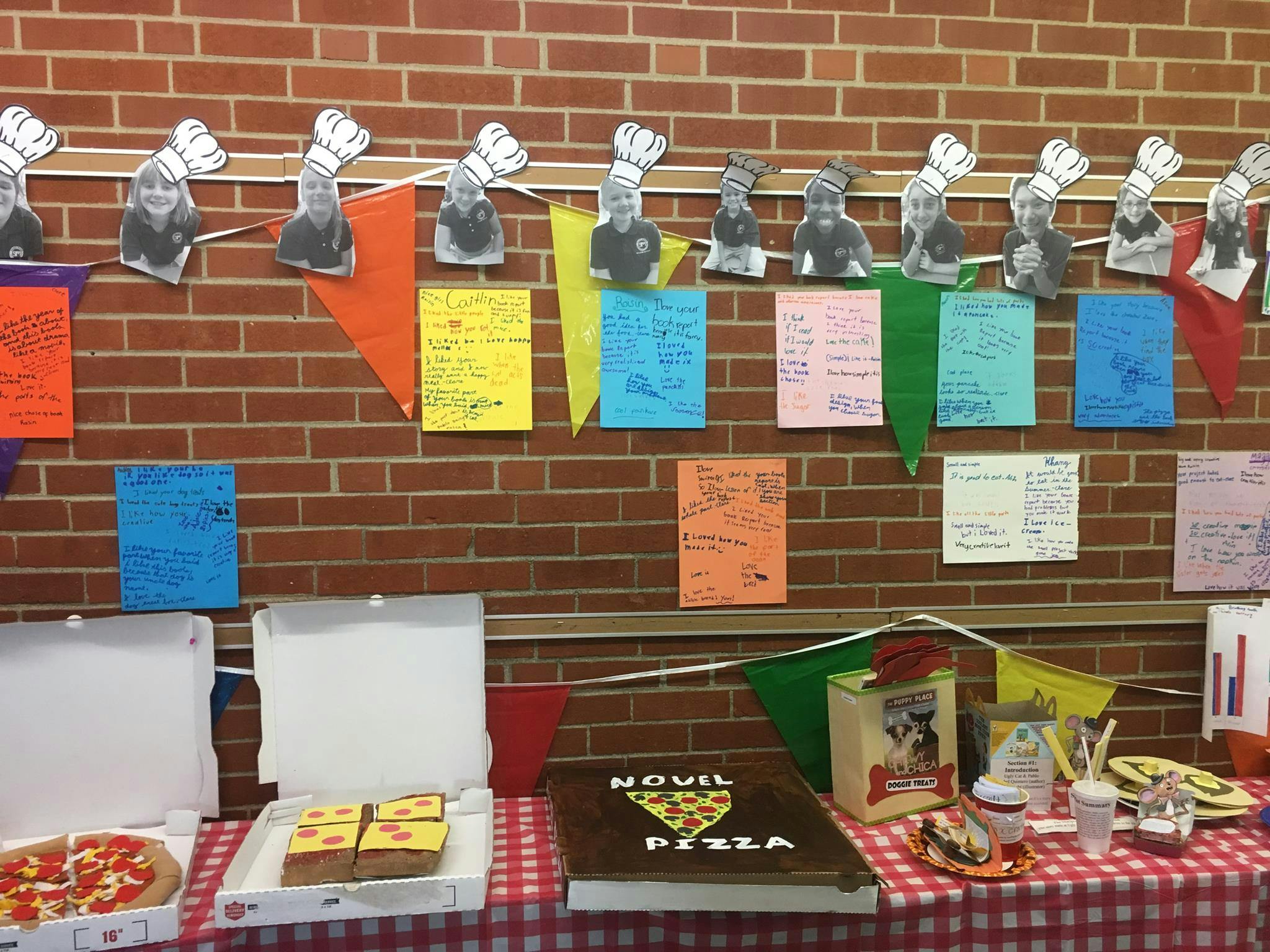 Pizza boxes and a book on a table with chef hat cutouts on a brick wall