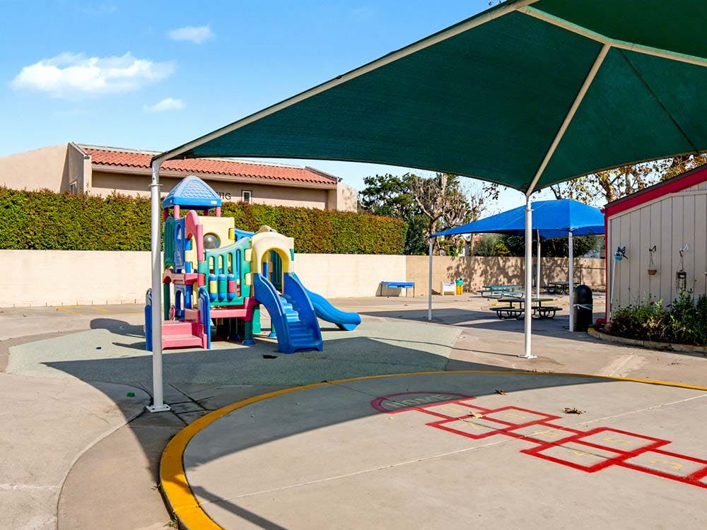 Colorful playground structure with slides and a hopscotch game on concrete