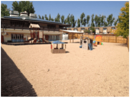 Outdoor playground with sand, play structures, and a building in the background
