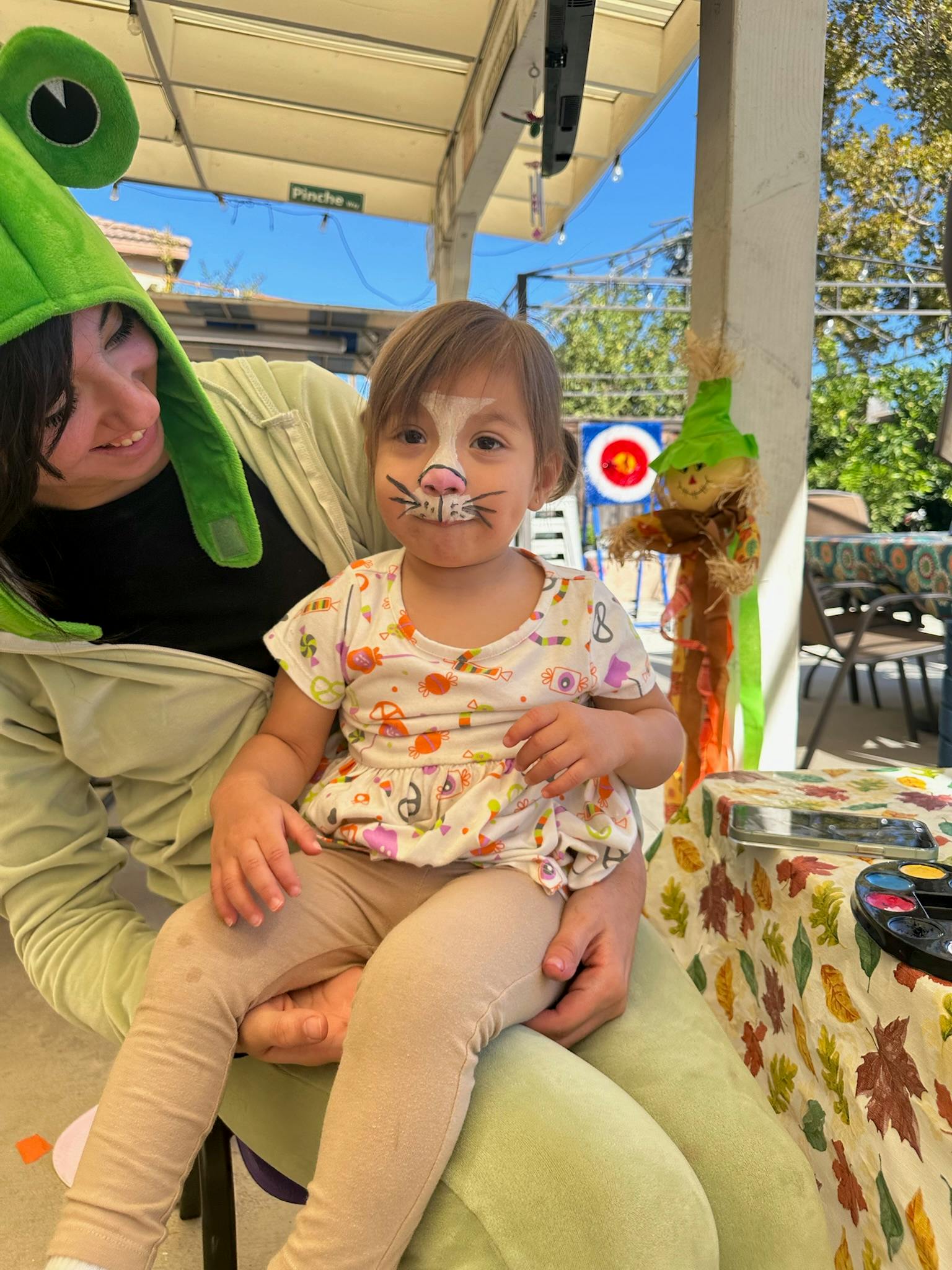 Person in frog hat holding child with painted face