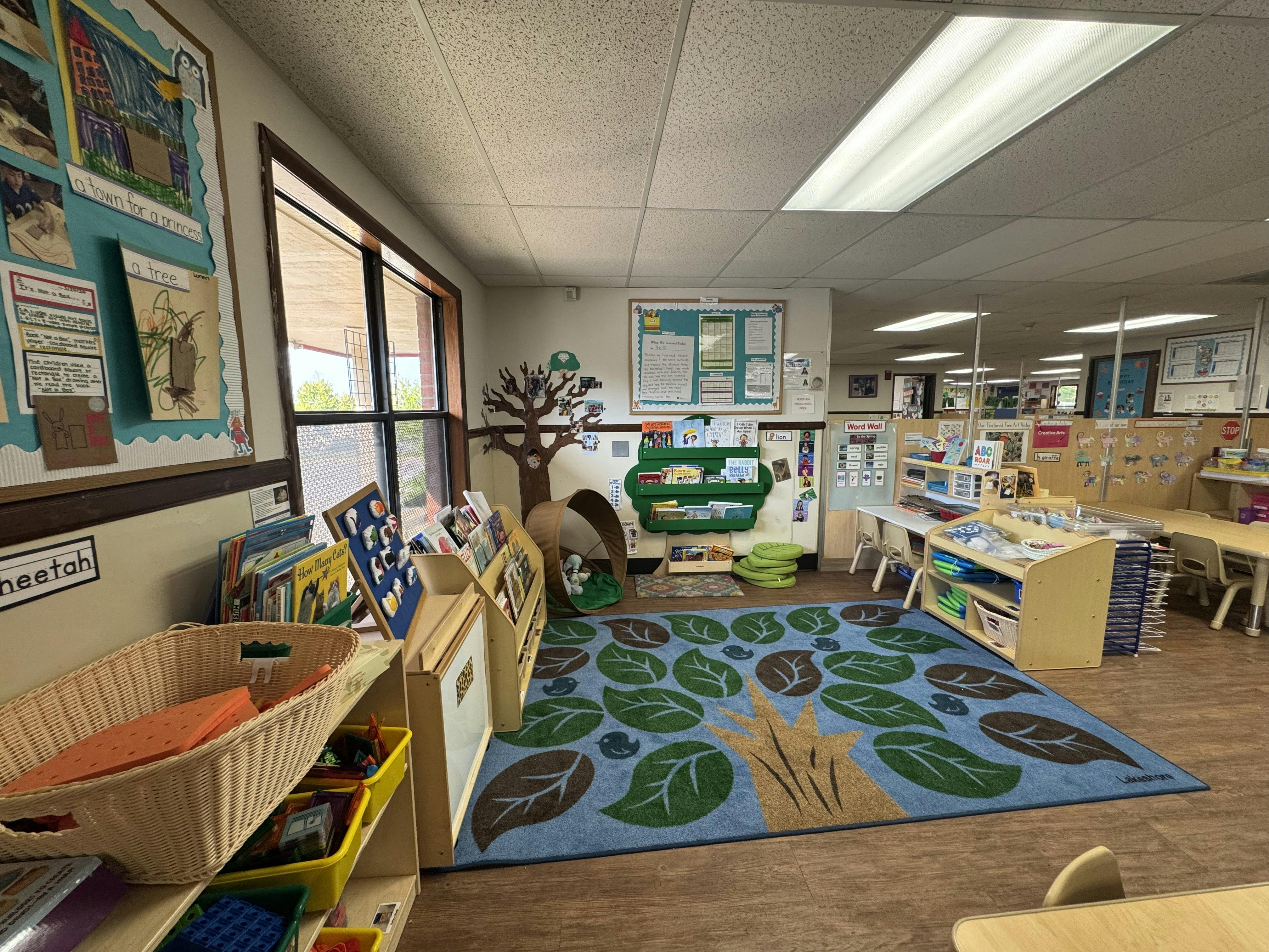 Classroom with a tree-themed rug, small furniture, and children's artwork on the walls