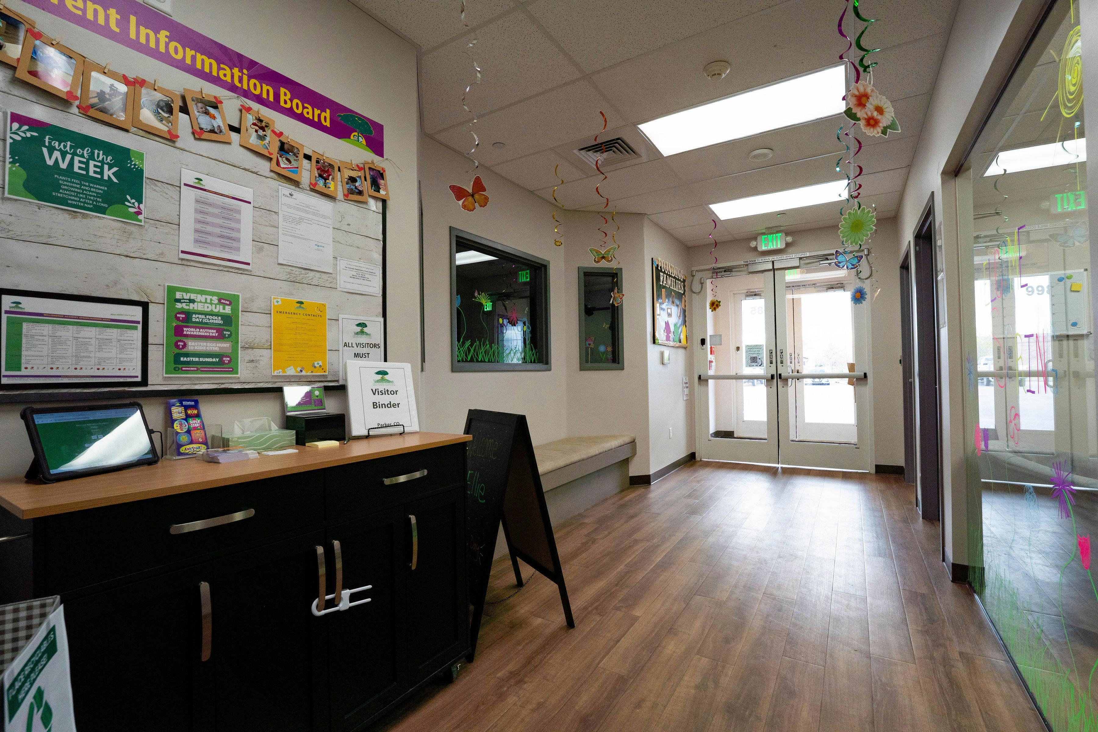 A hallway with a wooden floor, information board, visitor binder, and exit doors
