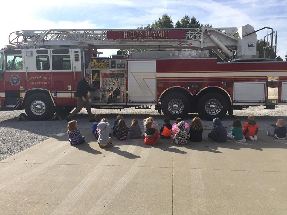 Children sitting on the ground in front of a fire truck