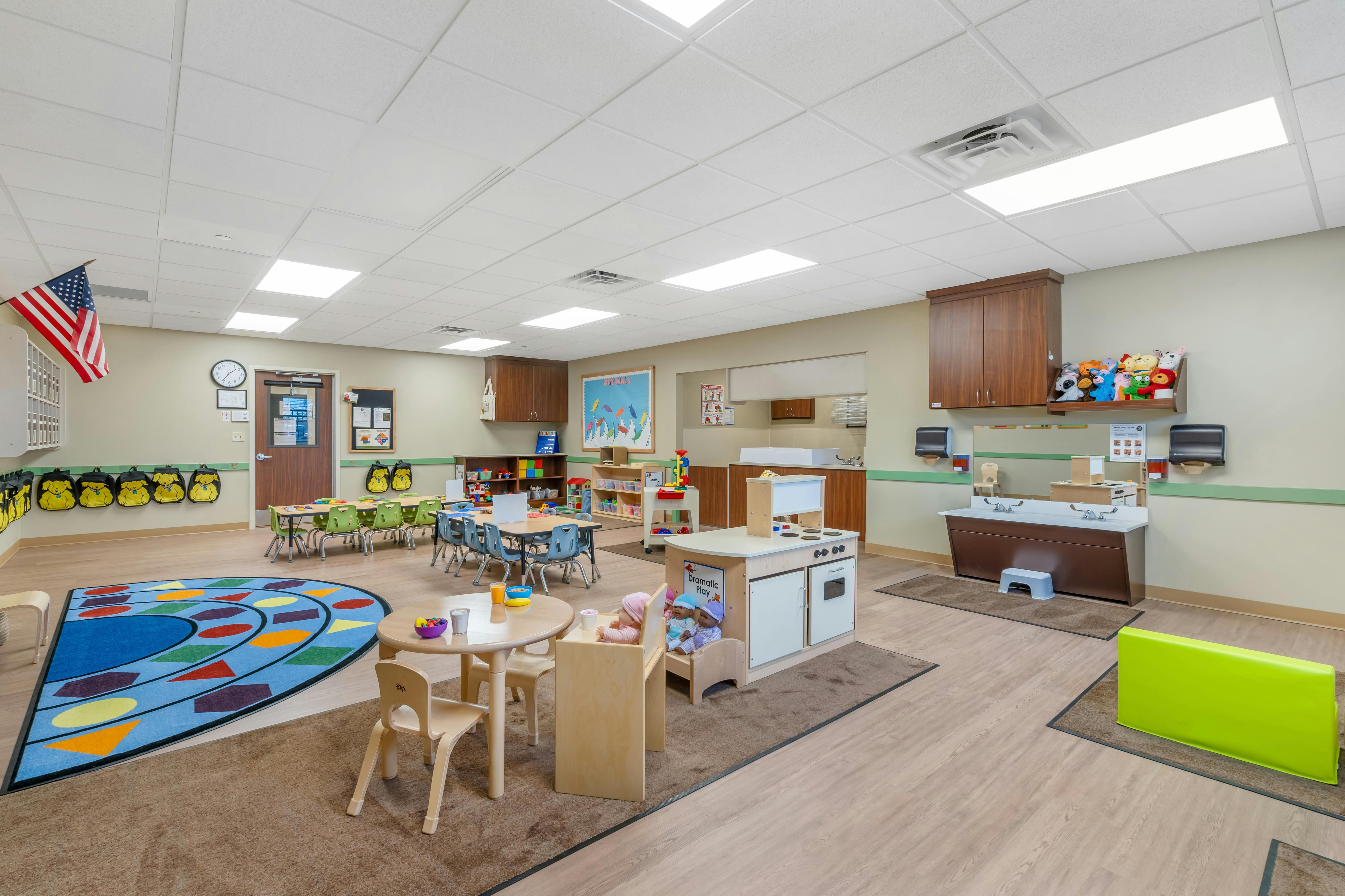 Classroom with small tables and chairs, play kitchen, and a colorful rug