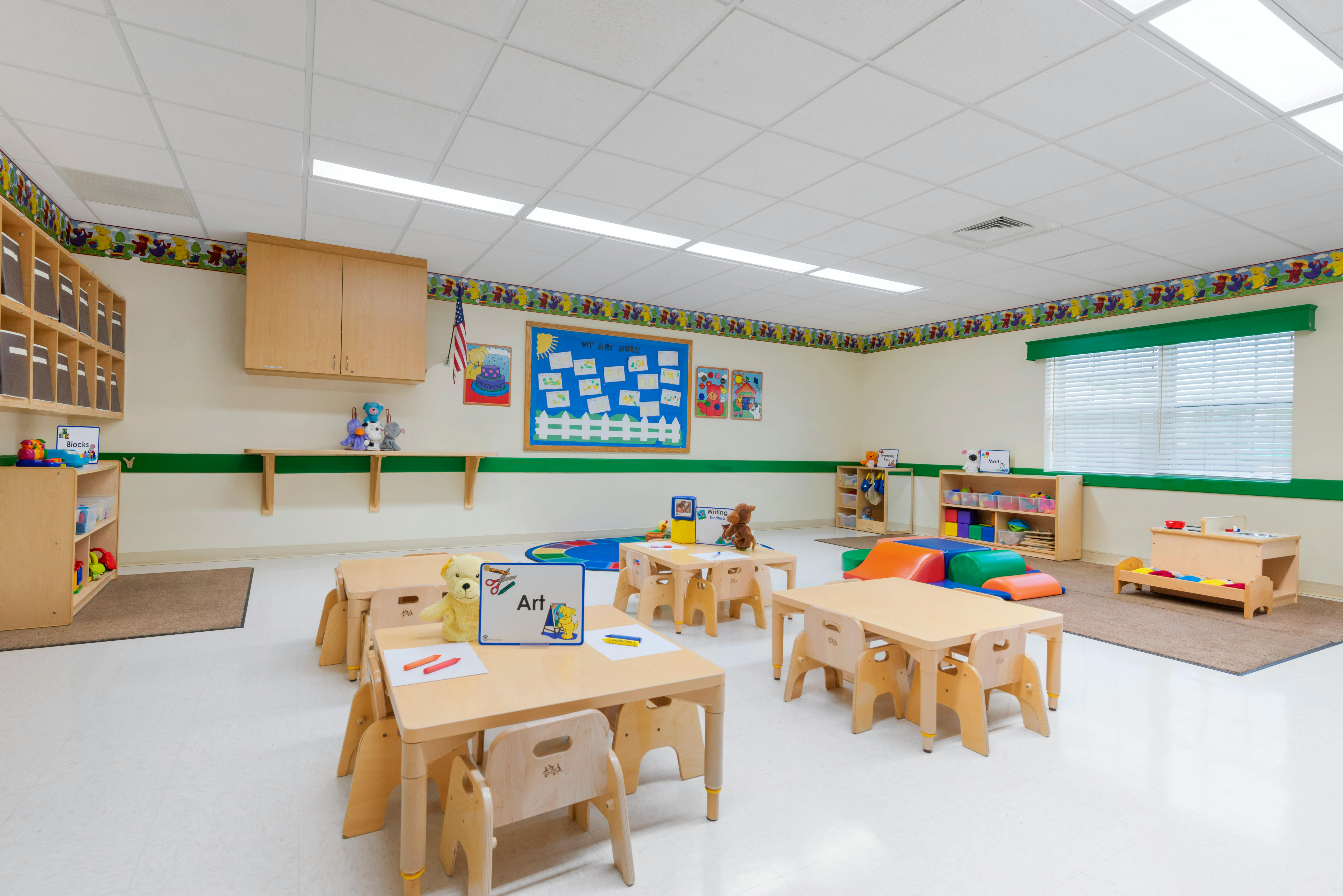 Classroom with small wooden tables and chairs, toys, and educational posters on the walls