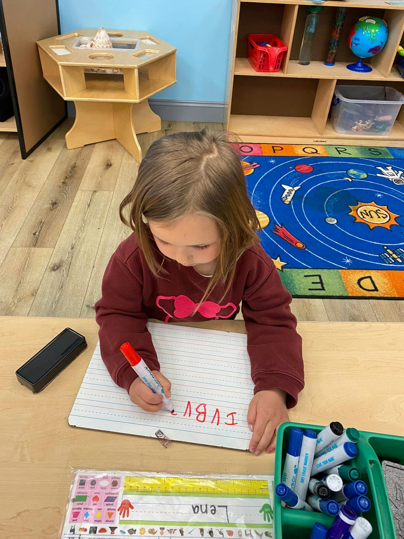 Child writing on a whiteboard with a red marker in a classroom