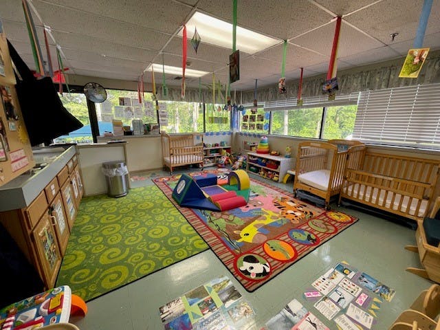 A colorful childcare room with cribs, play mats, and toys
