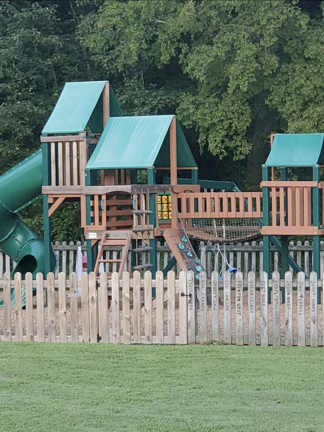 Playground structure with slides and swings behind a wooden fence