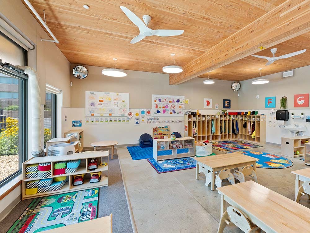 Classroom with small tables and chairs, cubbies, and colorful rugs