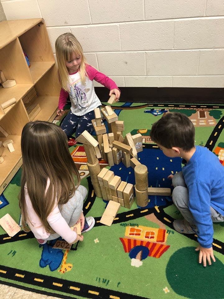 Three children playing with wooden blocks on a rug