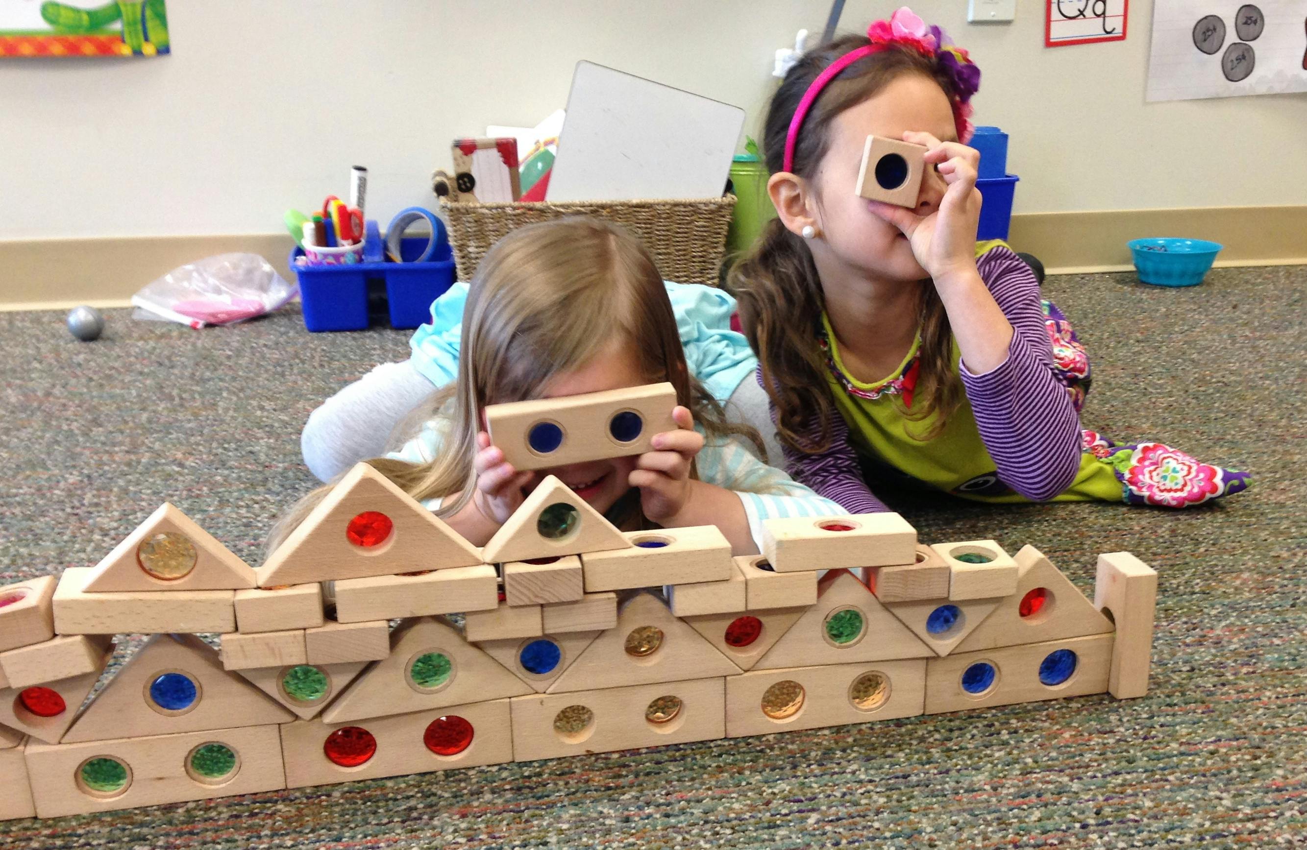 Two children lying on the floor playing with wooden blocks