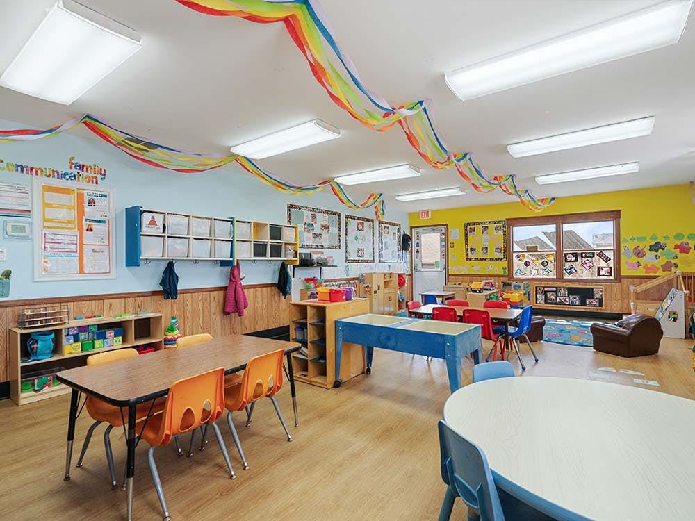 Colorful classroom with child-sized tables and chairs, shelves, and decorations