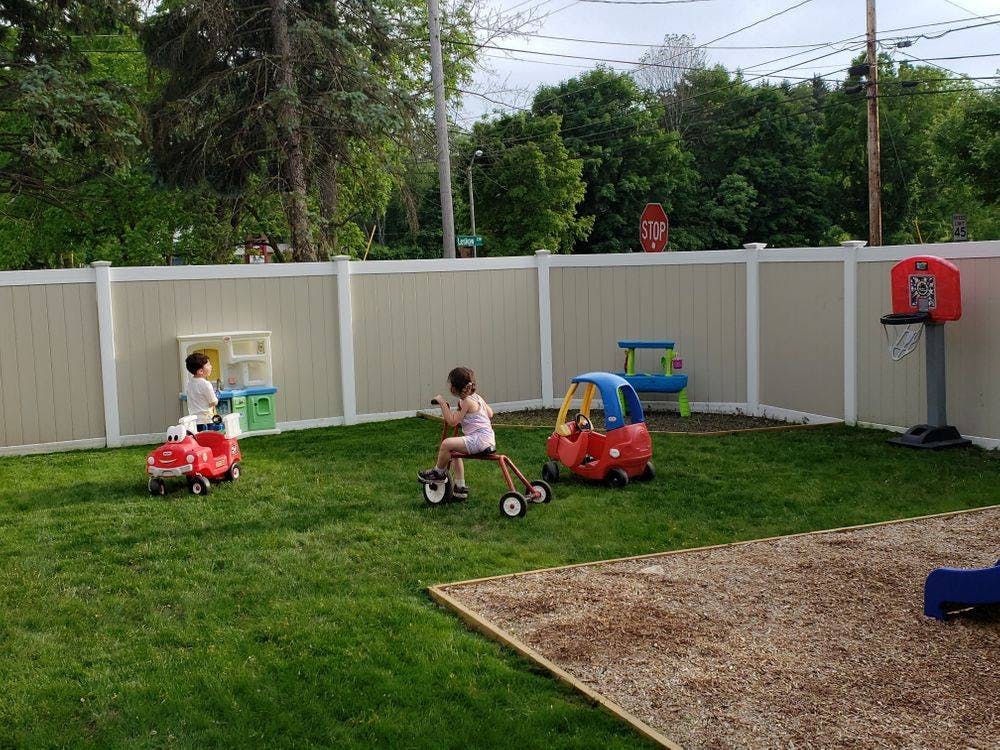 Two children playing with ride-on toys in a fenced yard