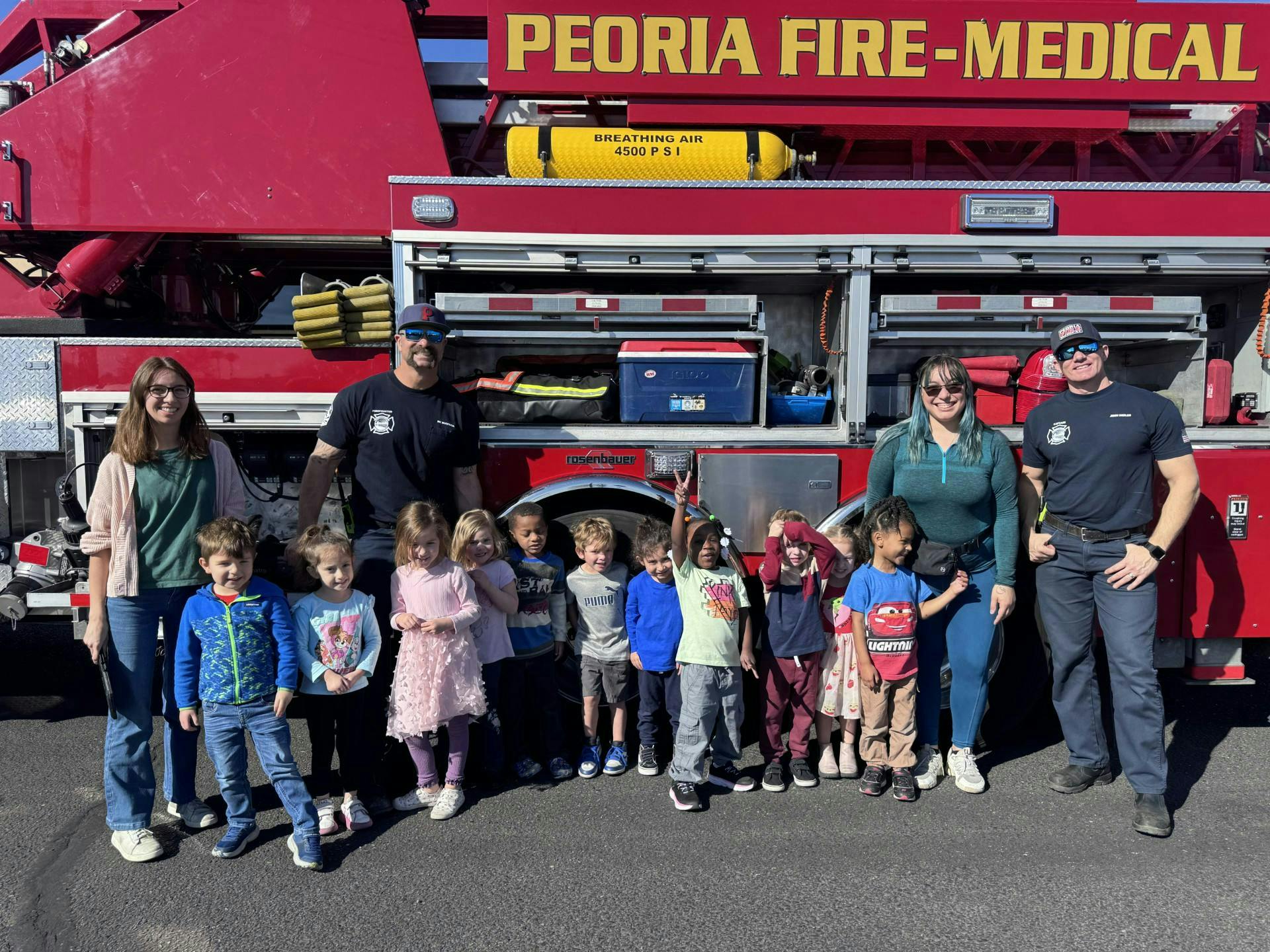 Adults and children posing in front of a fire truck with "PEORIA FIRE-MEDICAL" text