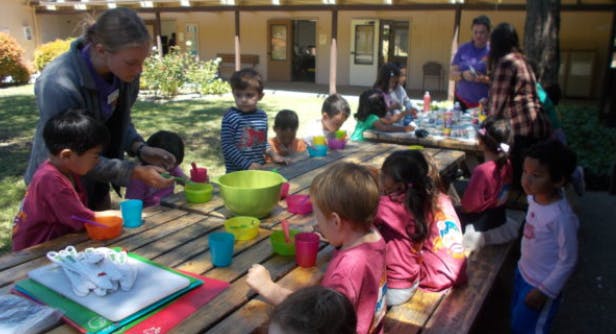 Adult and children gathered around a picnic table with colorful cups and bowls