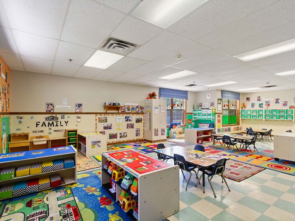Colorful classroom with small tables, chairs, and shelves full of toys and bins