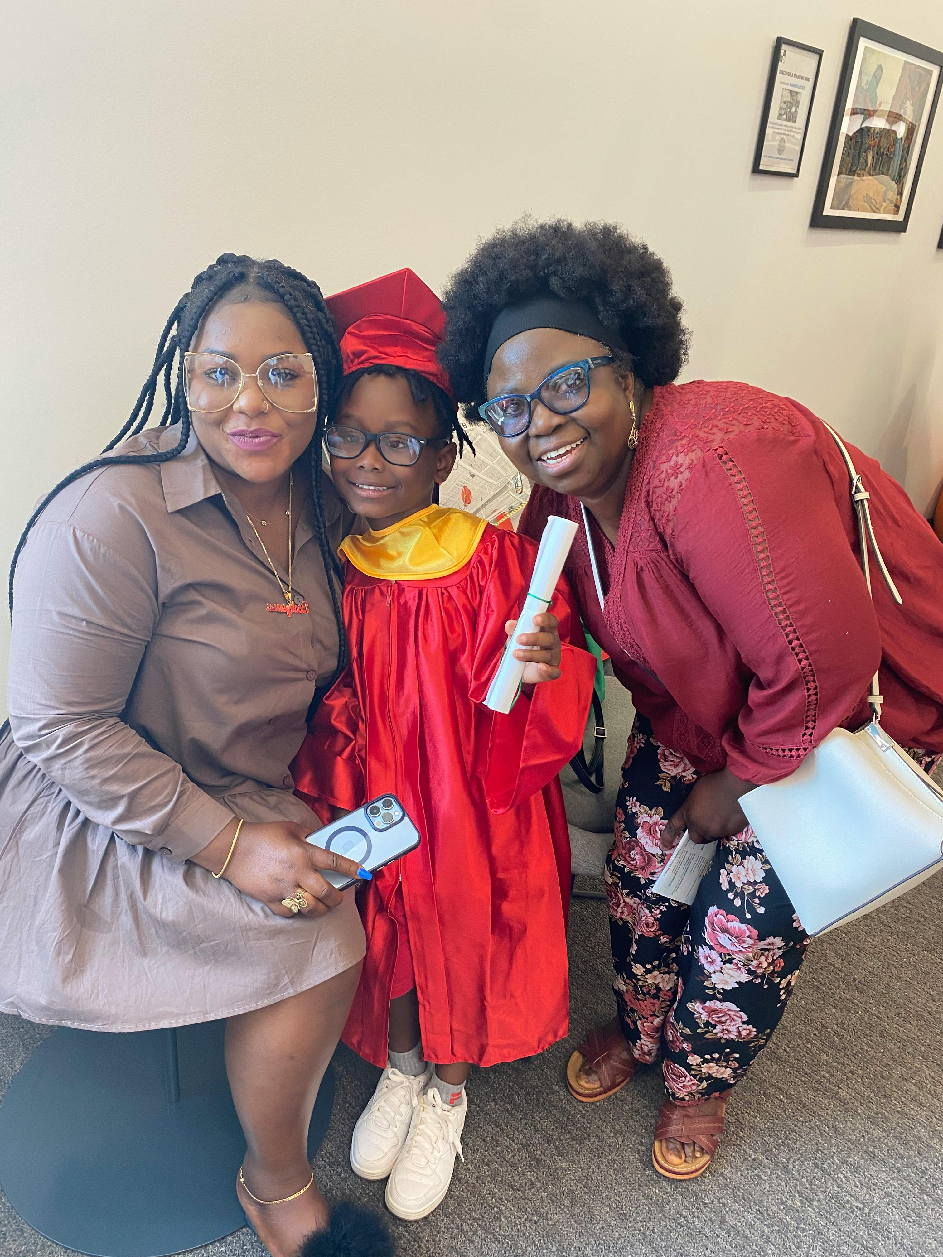 Two people with a child in a graduation cap and gown holding a diploma