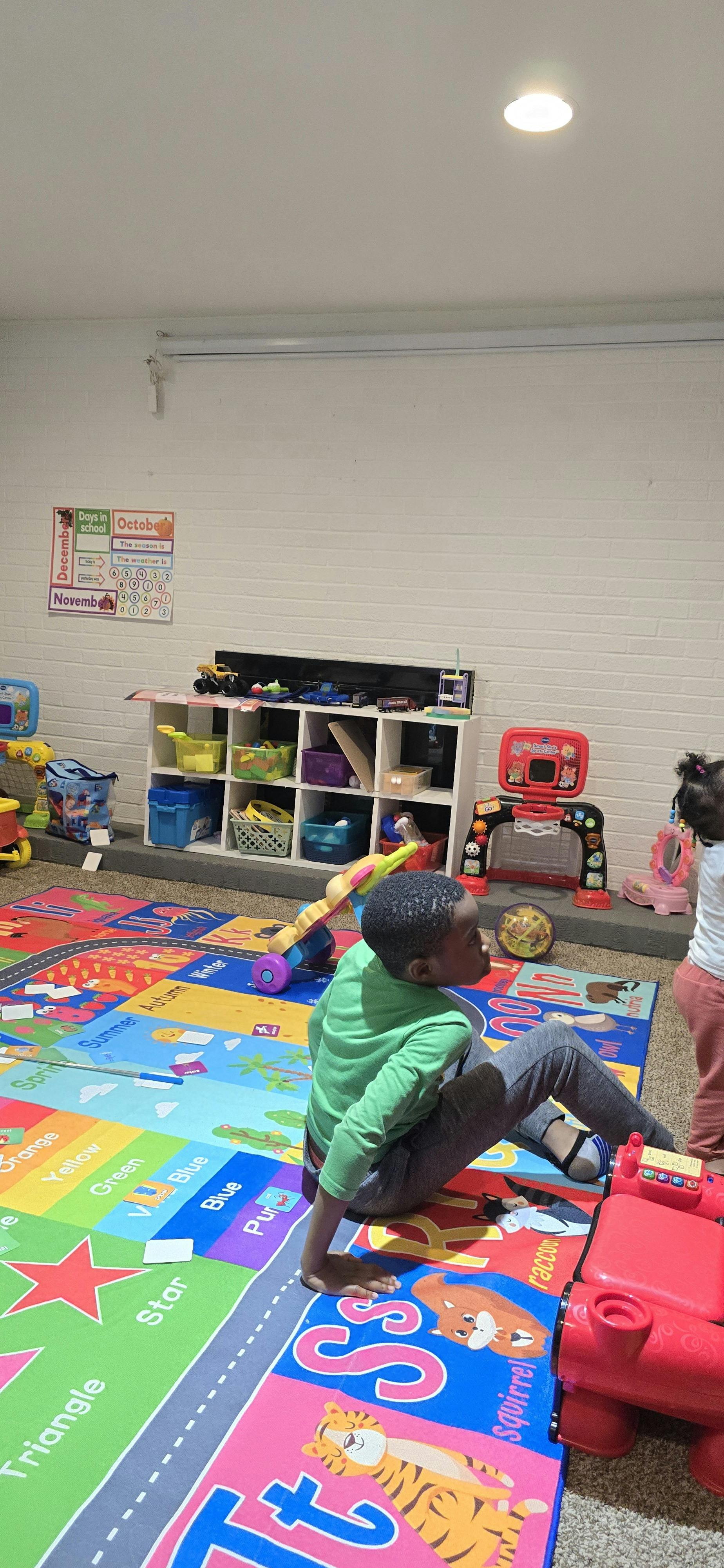 Child sitting on an ABC rug in a classroom filled with toys