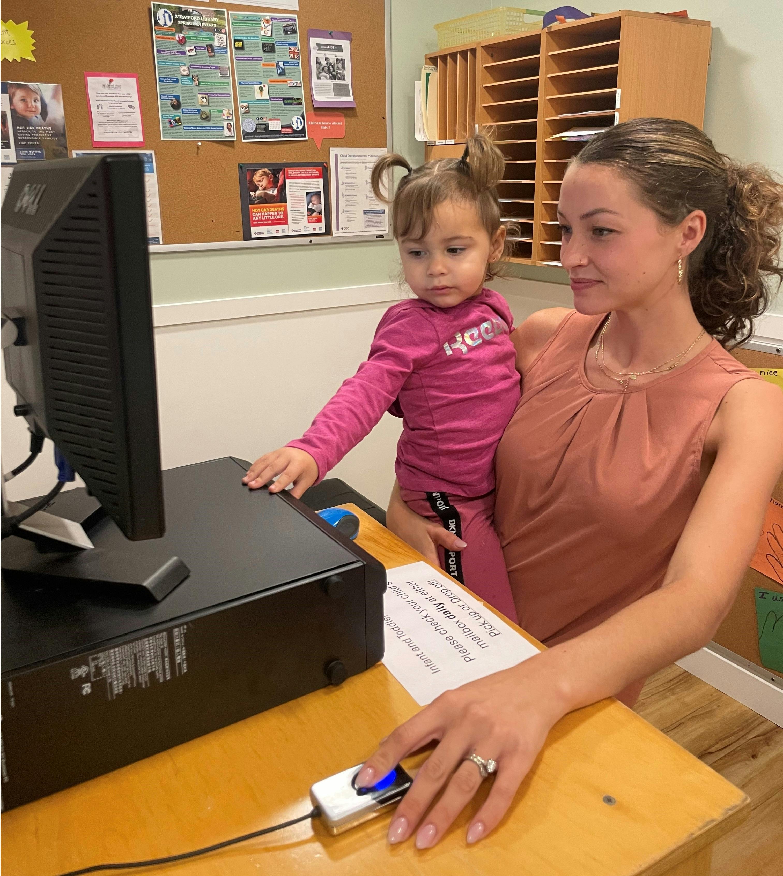 A person holding a child while using a computer at a desk