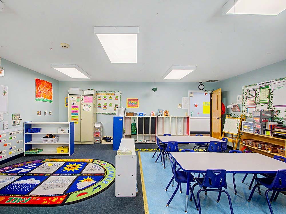 Colorful classroom with child-sized tables and chairs, and a large rug with seasons