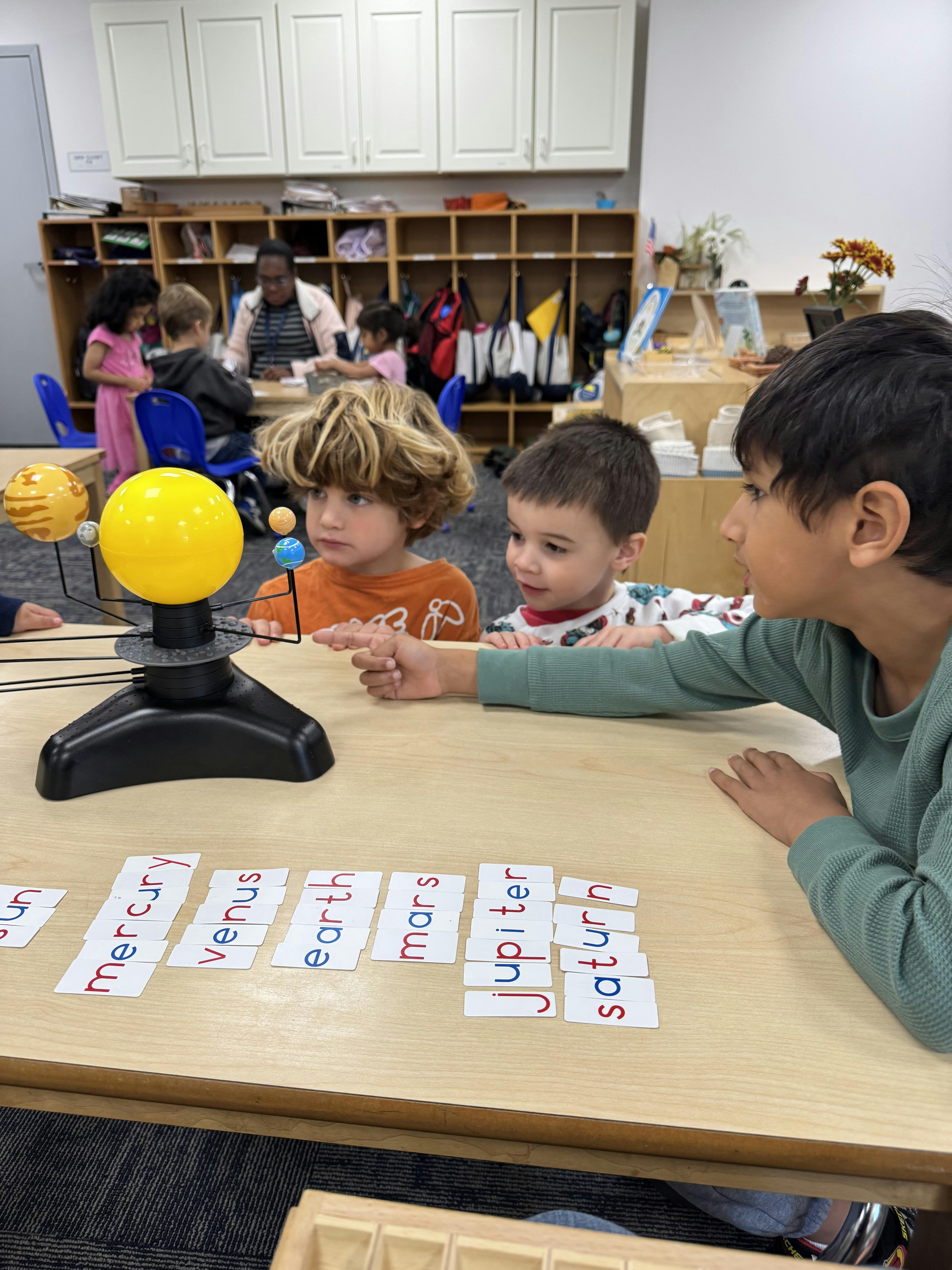Three children at a table with a solar system model and planet name cards