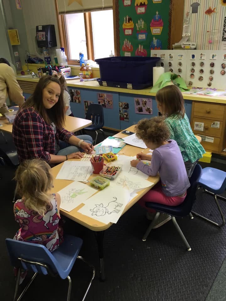 Adult and three children coloring at a table in a classroom