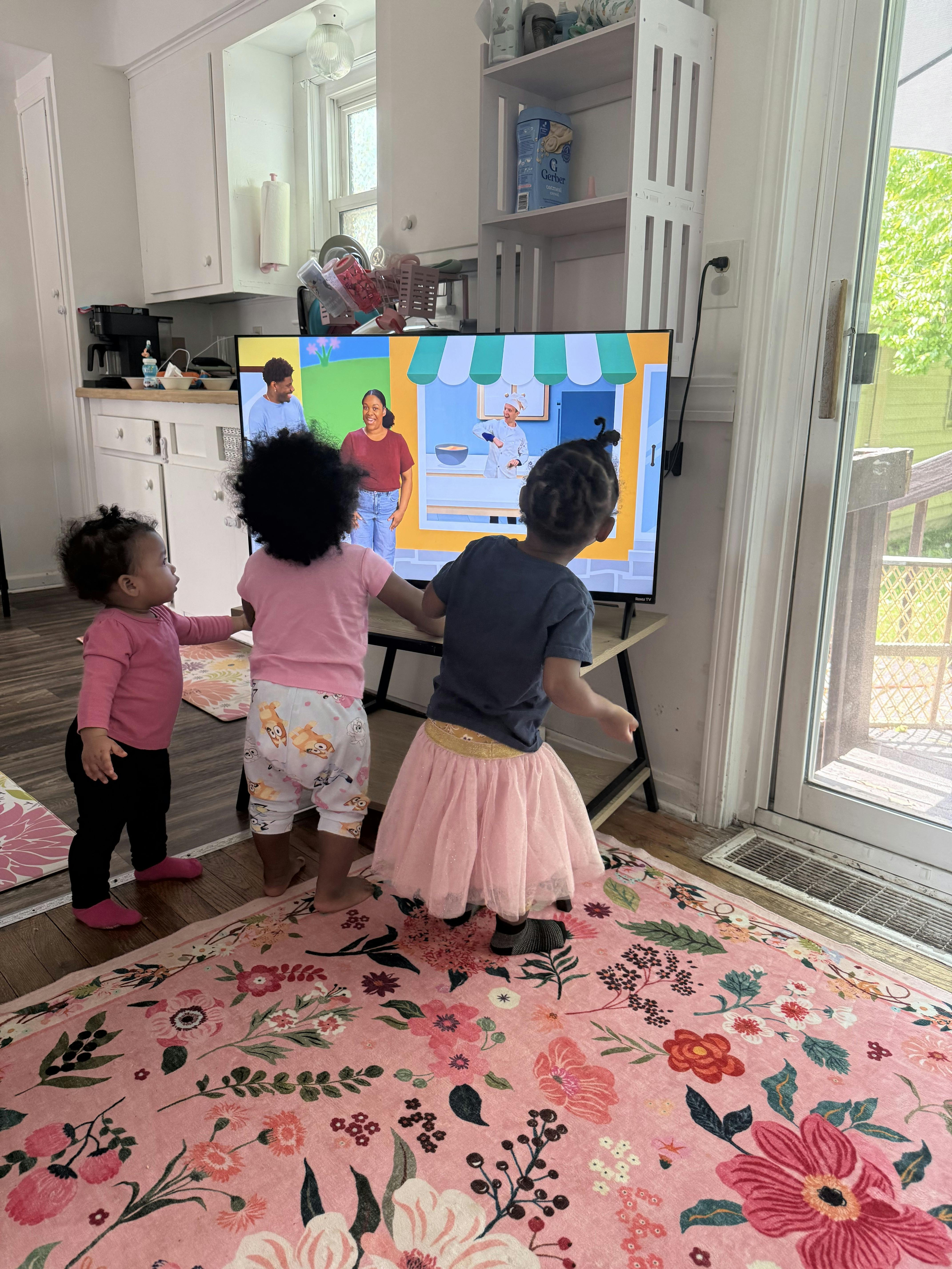 Three young children watching cartoons on a TV in a kitchen
