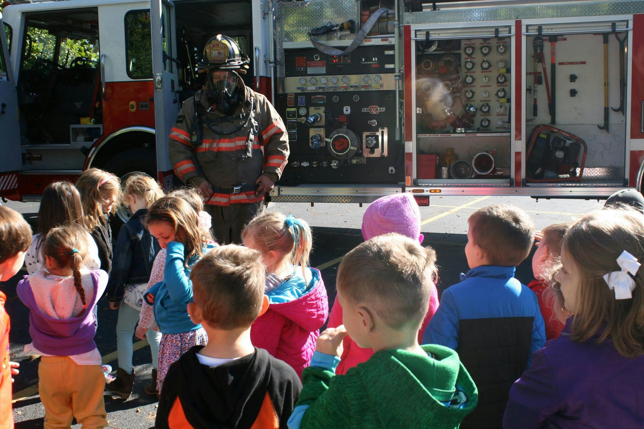 Firefighter in uniform standing in front of a fire truck with children watching
