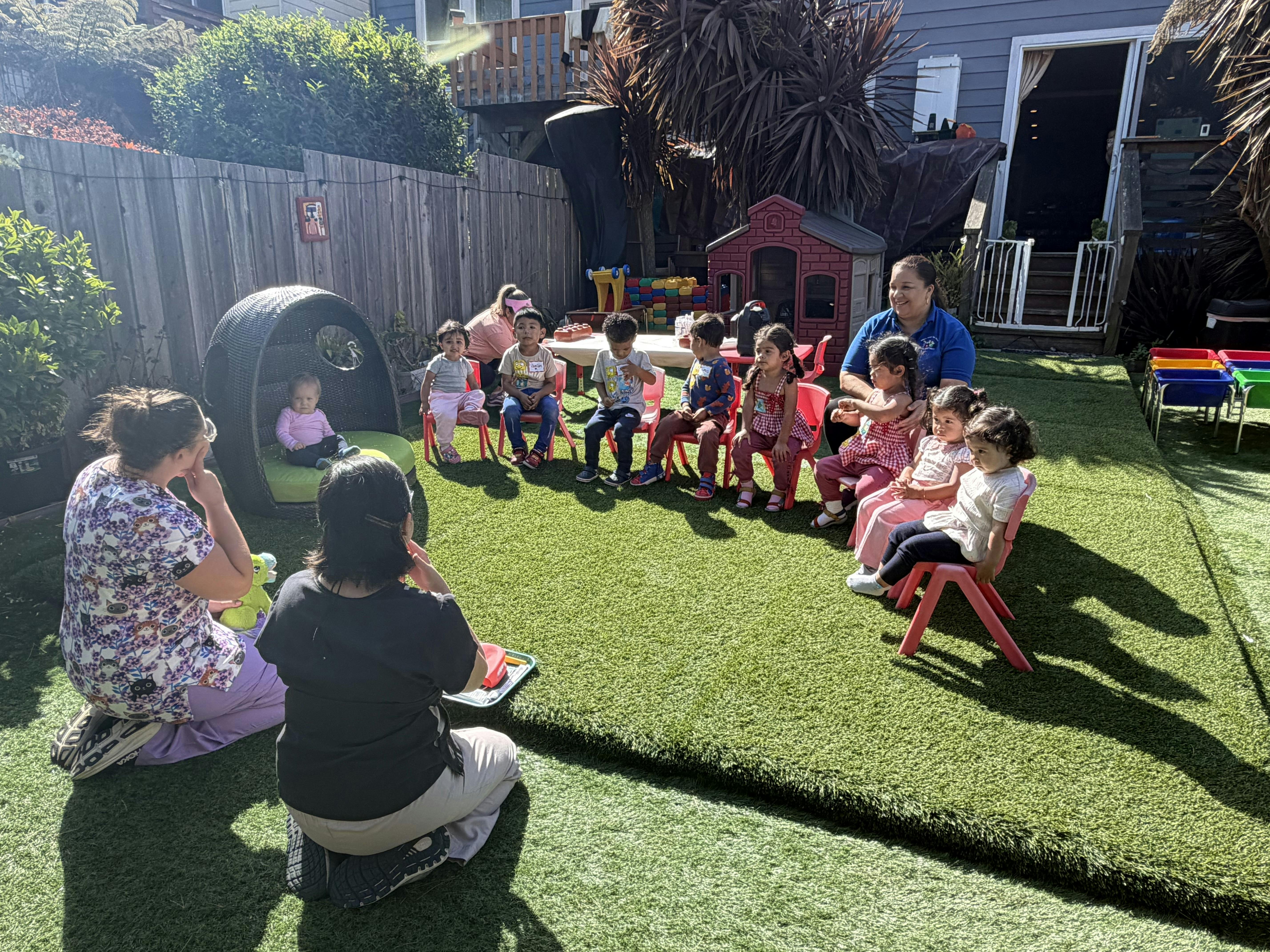 Group of children and adults sitting in a circle on an outdoor play area