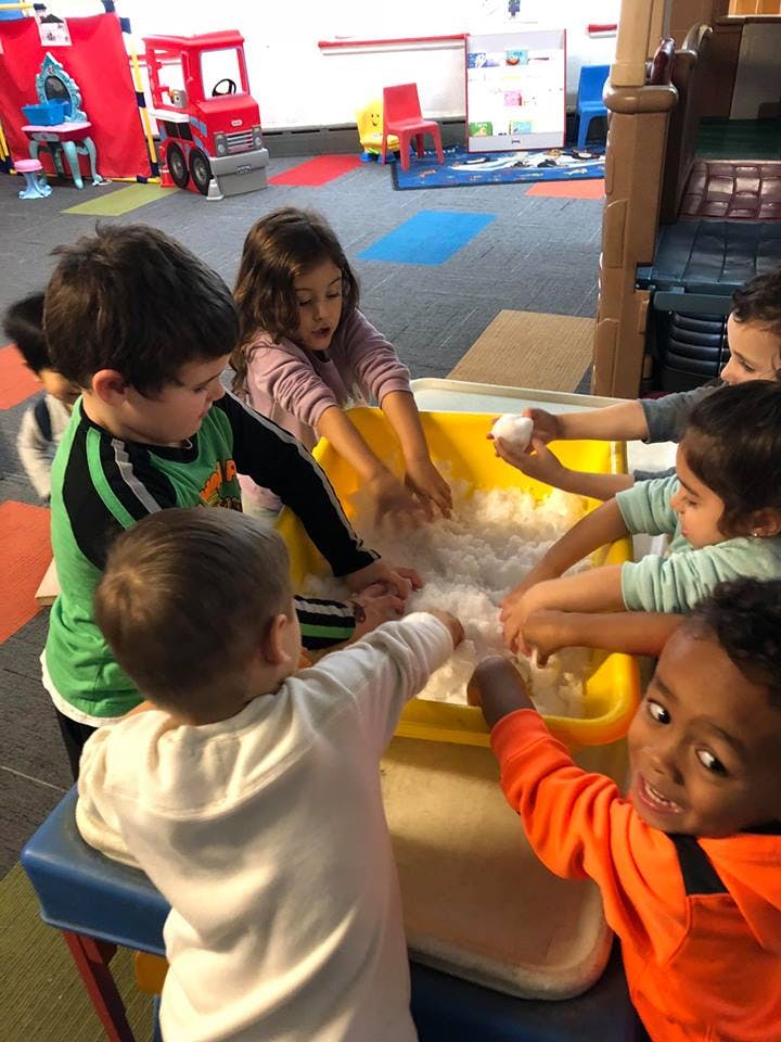 Children playing with white fluffy material in a yellow bin