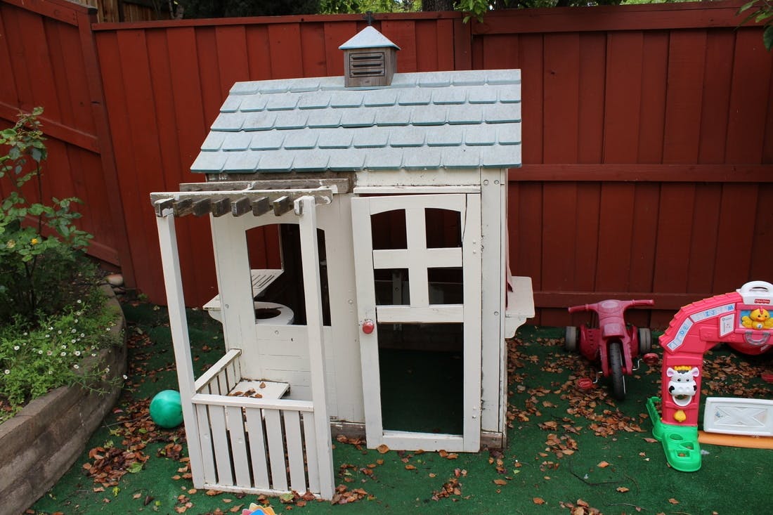 White playhouse with a blue roof in a yard
