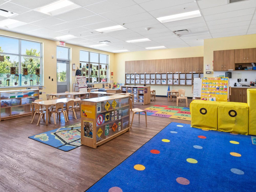 Empty classroom with small tables and chairs, colorful rugs, and storage cabinets