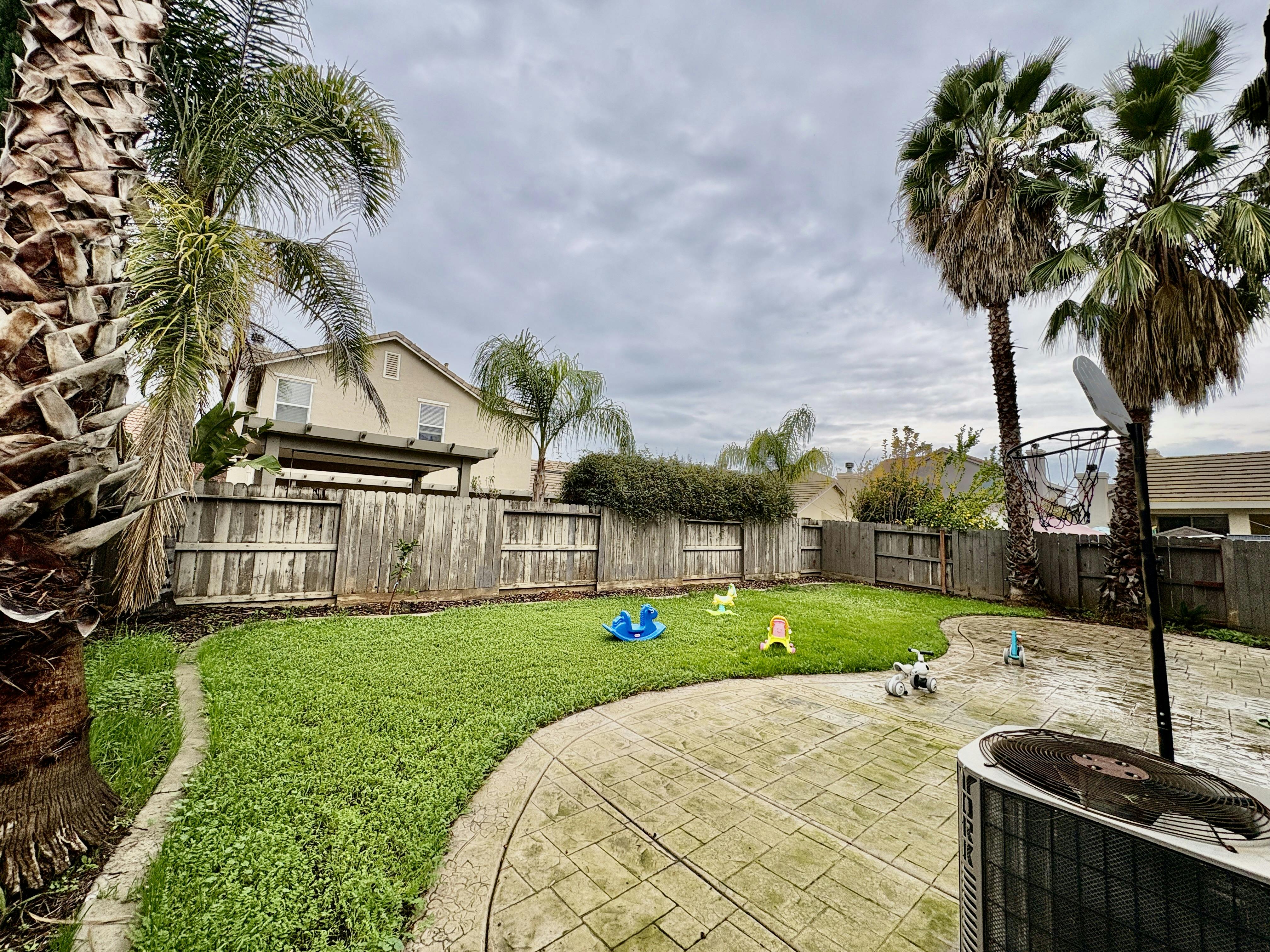 Backyard with green lawn, concrete patio, and wooden fence