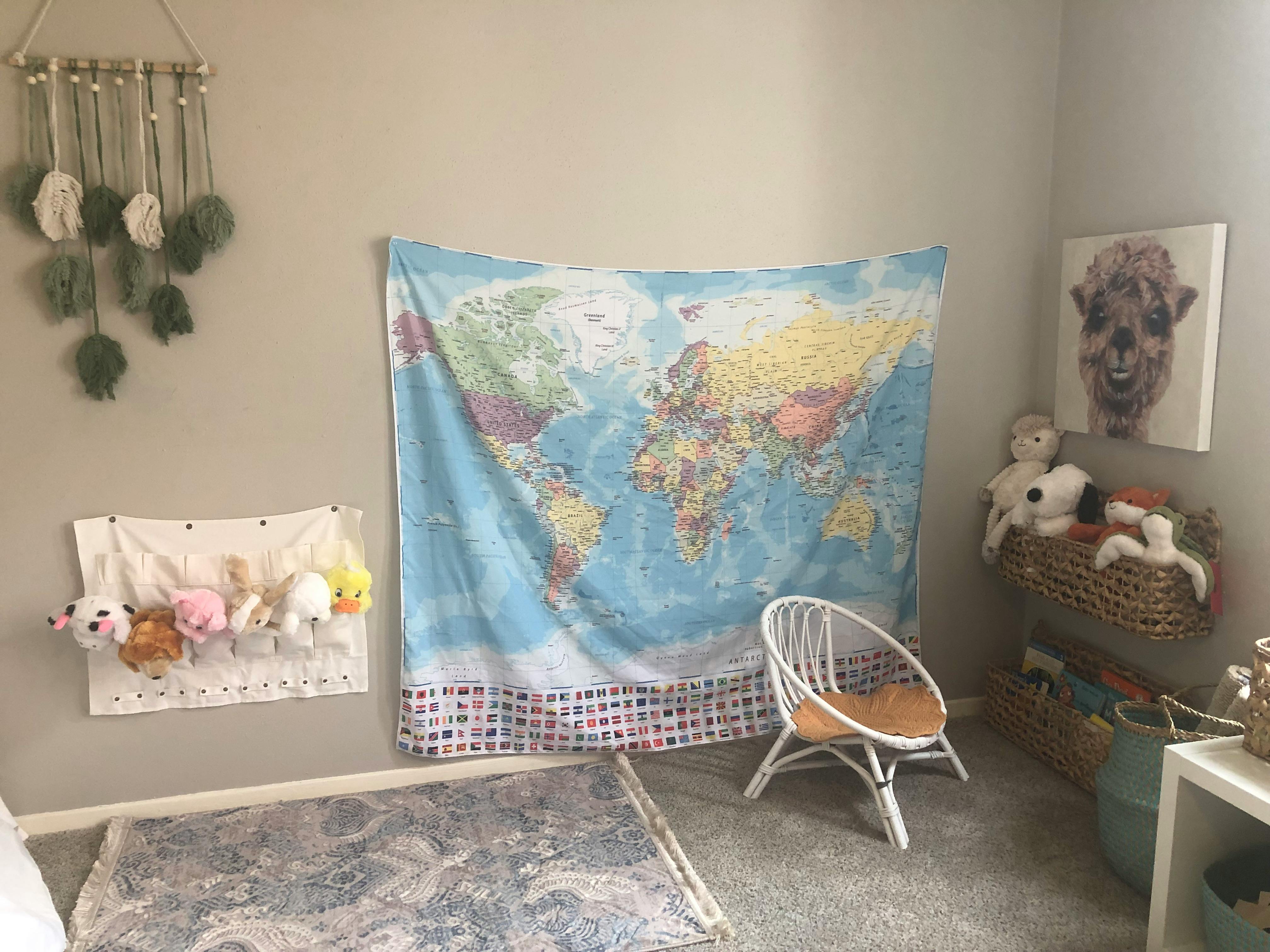 World map tapestry on a wall with a white chair and stuffed animals