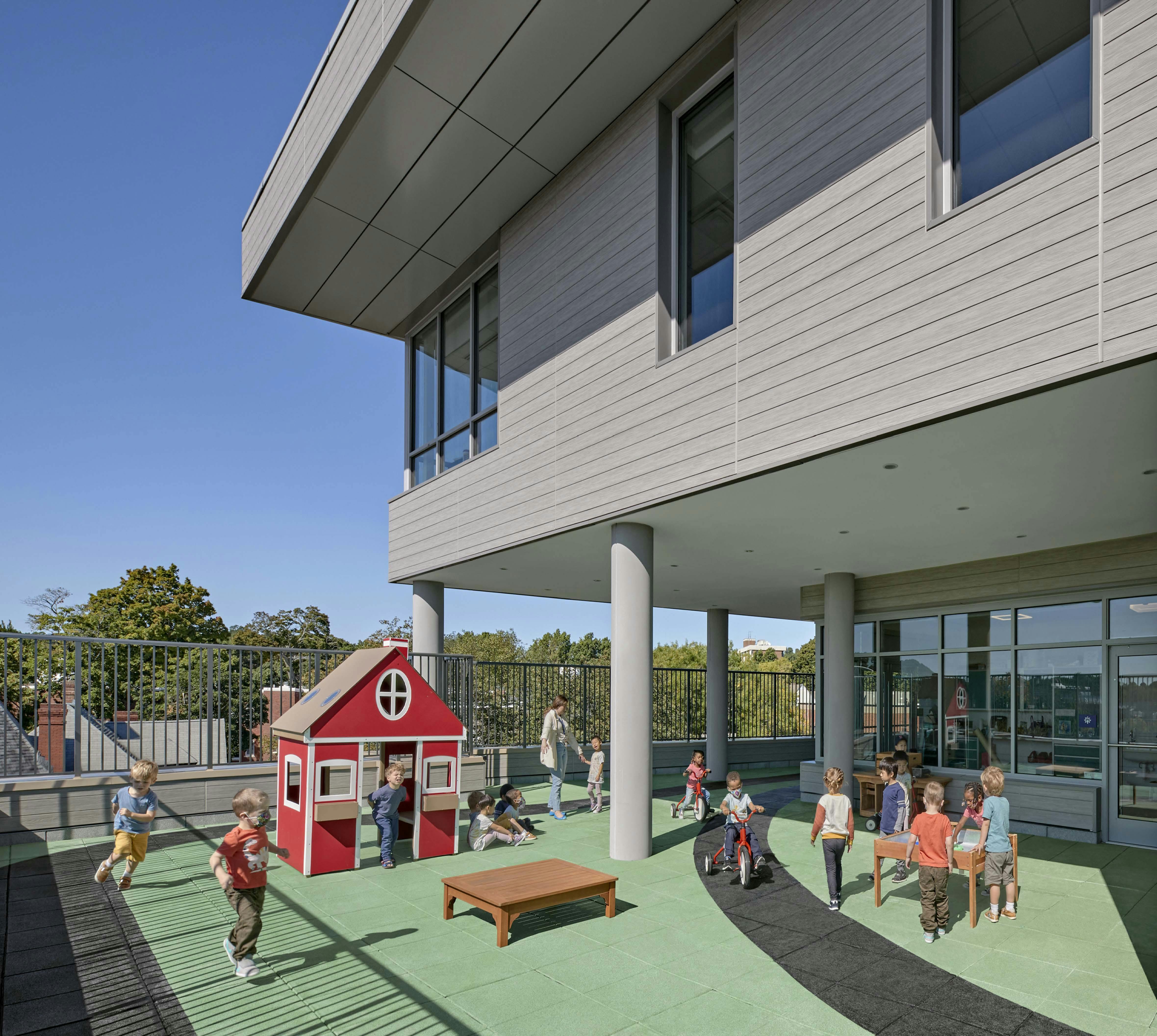 Children playing on a rooftop playground with a red playhouse
