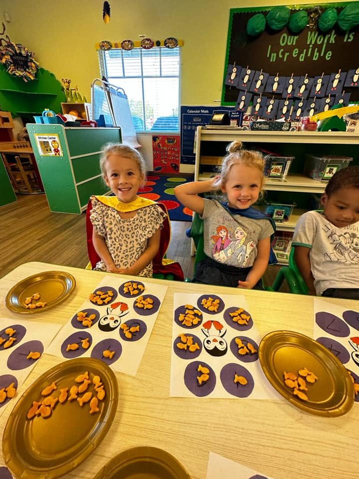 Three children sitting at a table with goldfish crackers and paper cutouts