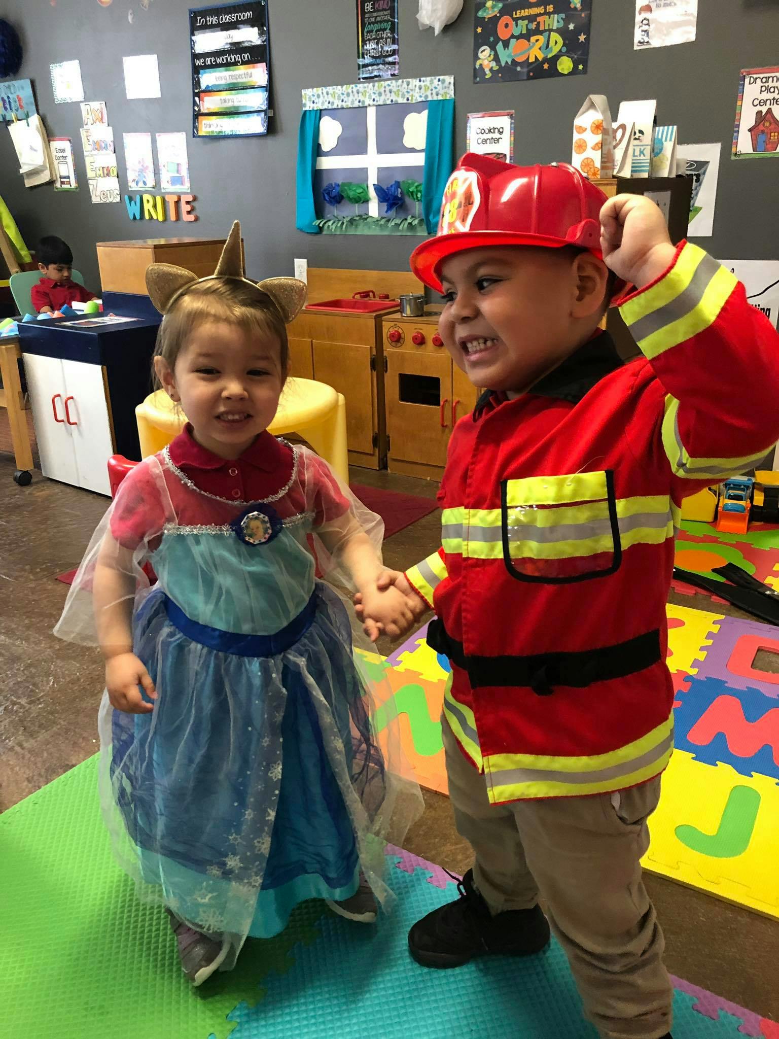 Child in firefighter costume holding hands with child in princess costume