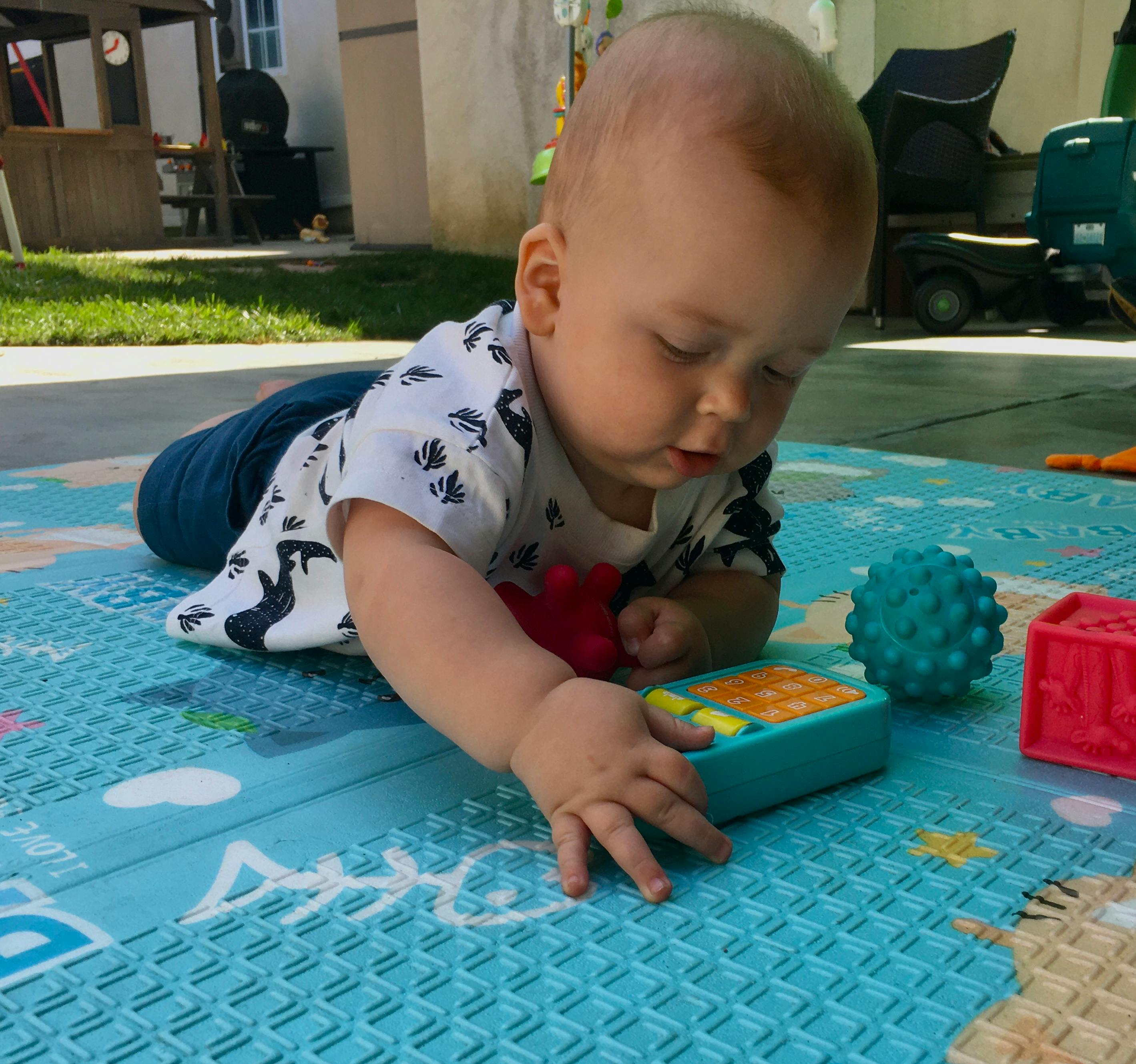 Baby lying on a play mat reaching for a toy phone