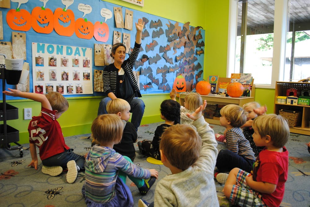 Person raising hand while children sit on floor in classroom